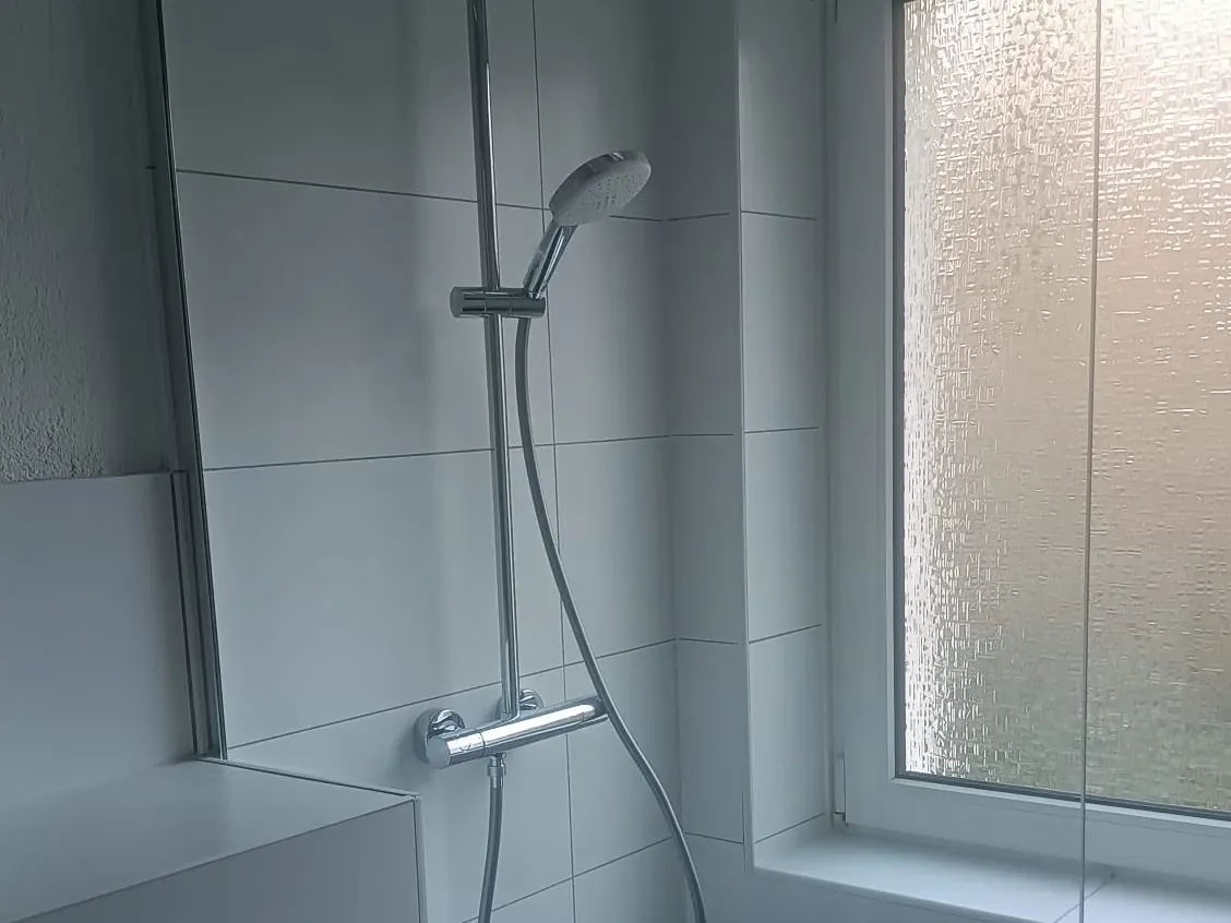 Neue bodengleiche Dusche mit weißen Fliesen und Thermostat-Armatur